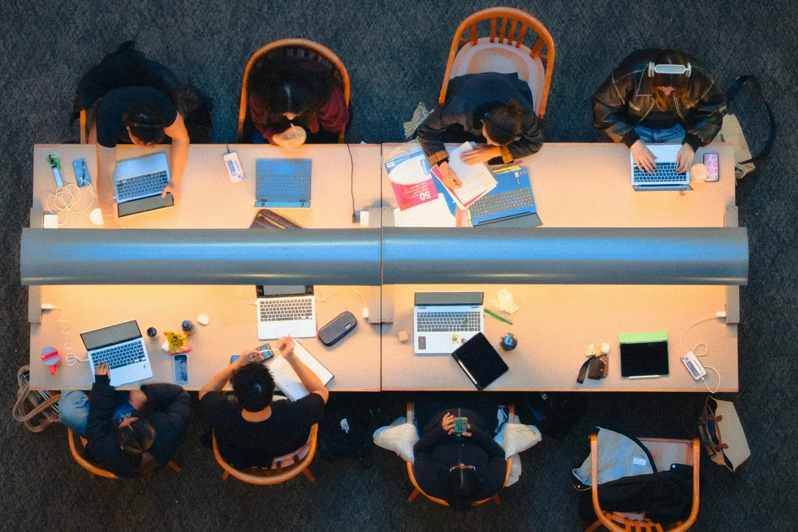 Students studying together at long tables in a university library, seen from above